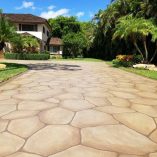 Decorative concrete driveway with large stone pattern leading to tropical house.