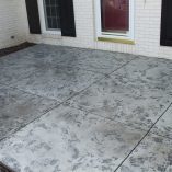 Stained and patterned concrete patio in grey tones with a red door in the background.