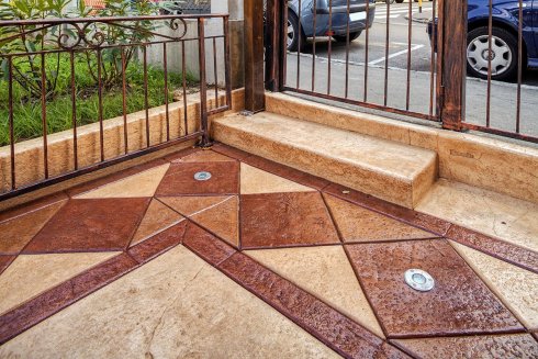 Decorative concrete porch with a geometric design in shades of brown and beige, next to a metal gate.