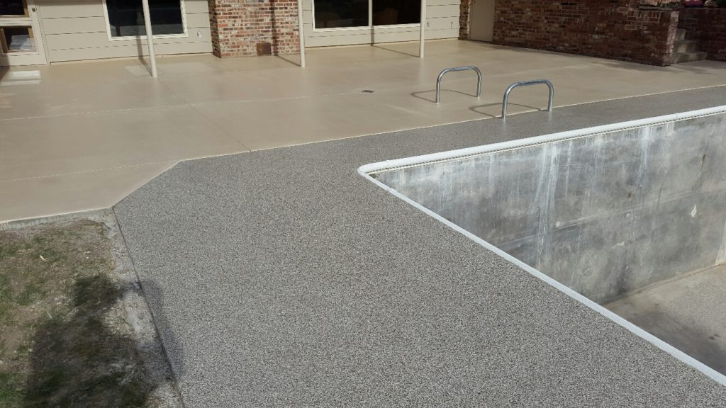 A concrete swimming pool deck with a speckled finish curves beside a pool, complementing the clean, modern lines of the surrounding architecture.