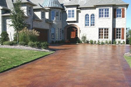 A grand stone house with large windows and a wooden door, featuring a spacious, russet-colored smooth concrete driveway.