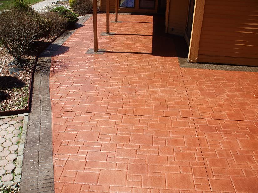 A brick-patterned stamped concrete walkway leading to a house, with landscaping on the side.