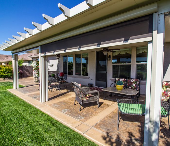 A comfortable patio area with stamped concrete flooring, a pergola, and cozy outdoor furniture surrounded by well-kept grass and a residential backdrop.